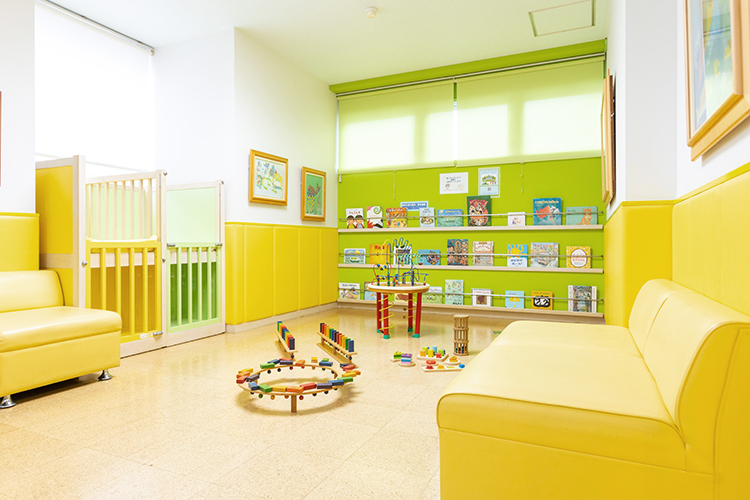 えびす子どもクリニック 北九州市小倉北区 床暖房完備のプレイルーム。木の玩具やたくさんの本が並ぶ